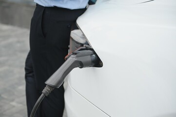Casual man with smartphone near electric car waiting for the finish of the battery charging process