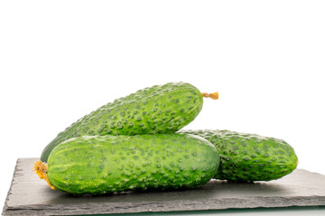 Three organic green cucumbers on a slate stone, close-up, isolated on a white background.