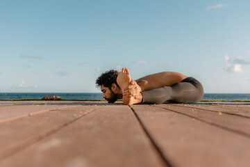 Young beautiful man practicing ashtanga yoga at sunset on the beach. Doing exercises and stretching. Wide Angle Seated Forward Bend Pose