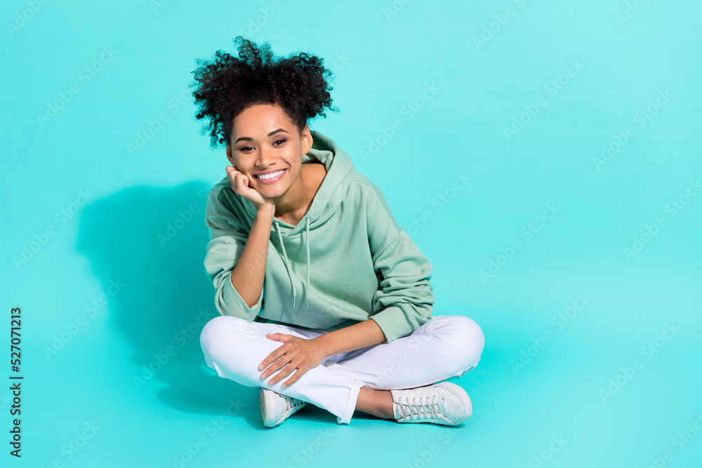 Wall mural Full length photo of adorable dreamy girl dressed hoodie sitting legs crossed hand arm chin empty space isolated teal color background