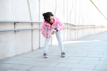 Young beautiful girl in pink sportswear with hood stretches outdoor