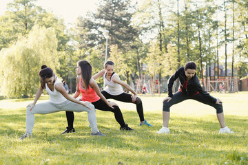 A group of healthy, beautiful, athletic women in sporty clothes stretching their legs in the park.