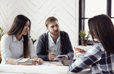 Fototapeta premium Three young colleagues working together on the project using pens and paper in the office
