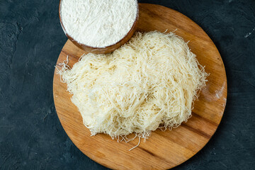 Kataifi dough from thin threads, round board, dark background, top view.
