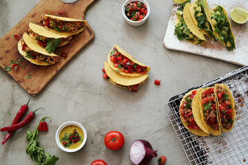 Many different fresh tacos with meat and vegetable fillings on a light surface
