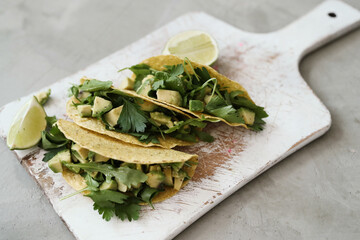Mexican taco with avocado and greenery on a wooden cutting board on light surface