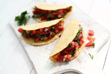 Traditional fresh Mexican tacos with sliced tomatoes and greens on a white cutting board