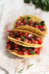 Three traditional fresh Mexican tacos with sliced tomatoes and greens on a white cutting board