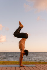 Fototapeta na wymiar Young beautiful man practicing ashtanga yoga at sunset on the beach. Doing exercises and stretching.
