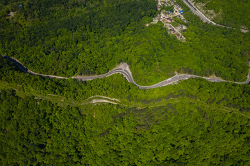 Aerial view of winding road from the high mountain pass. Great road trip trough the dense woods. Birds eye view.