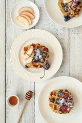 Top view of Belgian waffles with berries and powdered sugar on a wooden surface.
