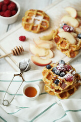 Belgian waffles with berries and powdered sugar on a wooden surface.