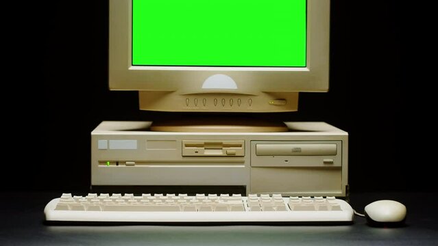 Old computer with green chroma key screen close-up, Desktop PC isolated on black background. Retro obsolete technology. 