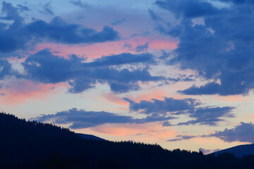 Pink glow on high clouds after sunset with foreground treeline in shadow