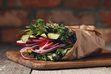 Fresh, tasty vegetable sandwich wrapped in paper on a wooden cutting board