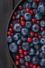  Summer blueberries and red currants on a black plate on a dark wood background. Fresh healthy summer food concept