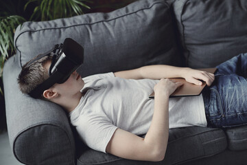 Obraz premium Teen lies on the couch and plays with glasses of virtual reality at home
