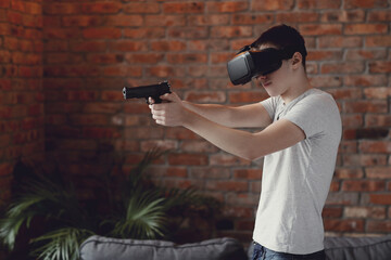 Teen playing with virtual reality glasses with toy gun in hands