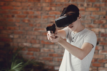 Teen playing with virtual reality glasses with toy gun in hands