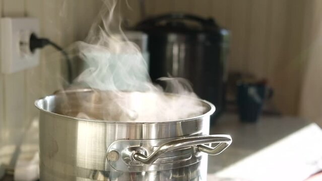 Saucepan on gas stove with steam jet rising. Boiling water with steam in a pot on electric stove in the kitchen. Blurred background. Cooking. The pot on gas burner. Close-Up Of Steaming Pot In Kitchen