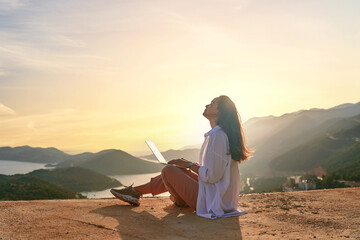 Free happy inspired freelancer girl enjoys remote works at a computer at sunset with beautiful...
