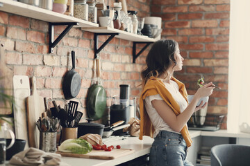 A young, beautiful, charming woman eats fresh vegetable salad in the kitchen at home