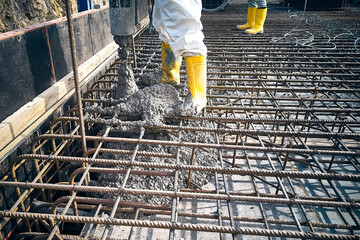 Contractor is casting concrete using concrete pump tube. Cement works on a construction site. Construction workers dressed in uniform pour a concrete to formwork - obrazy, fototapety, plakaty