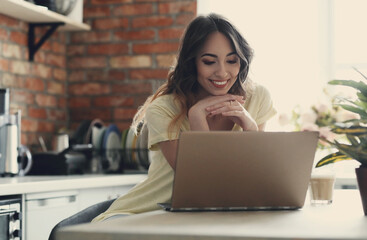 Young, charming, brunette girl watching a movie on the computer in the kitchen at home