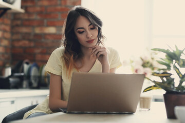 Young, charming, brunette girl watching a movie on the computer in the kitchen at home