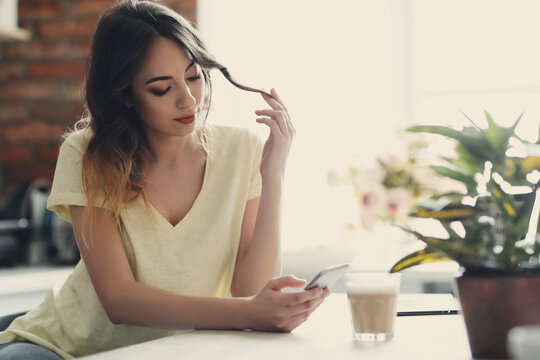 Young, charming, brunette girl holding modile phone in the kitchen at home