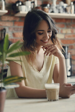 Young,brunette woman holding her morning cup of coffee on her hand and sitting at the kitchen
