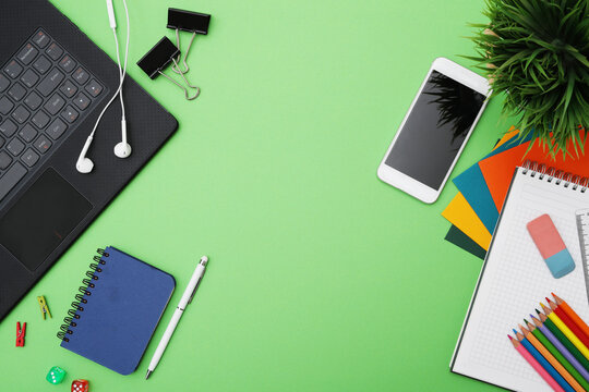 Top view of different stationeries with computer and mobile phone isolated on a green background