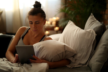 A woman with a bun on her head lying in bed with a tablet 