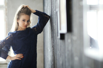 Beautiful, young girl in a short dress stands with her hand against the wall and poses for the...