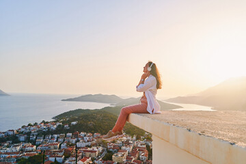 Inspired happy female sitting on top and enjoying of listening calm music with beautiful view at...