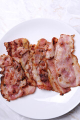 Top view of hot fried bacon slices in a white plate