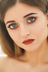 Close-up portrait of a young,blonde,naked woman with bright makeup and blue eyes on a white background