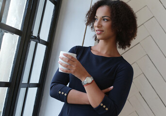 Close-up image of a smilng,beautiful woman with curly hair holding a cup of beverage