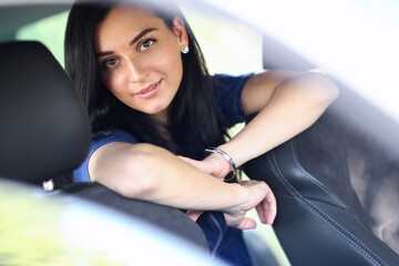 Photo of a young, brunette woman in a blue dress posing for a camera in her car