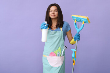 Portrait of a middle age woman in blue gloves  holding in her hands cleaning products while...