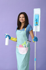 Portrait of a middle age woman in blue gloves  holding in her hands cleaning products while standing on a purple background.