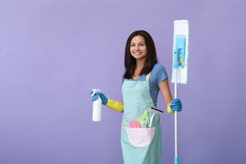 Portrait of a middle age woman in blue gloves  holding in her hands cleaning products while standing on a purple background.