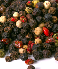 Black, red, white, and green peppercorns on a white background. 
