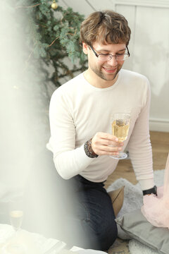 A young,beautiful man sitting on the white,fluffy carpet and holding a glass of wine at the party