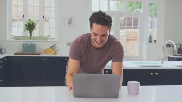 Transgender Man Working From Home Looking At Laptop On Kitchen Counter