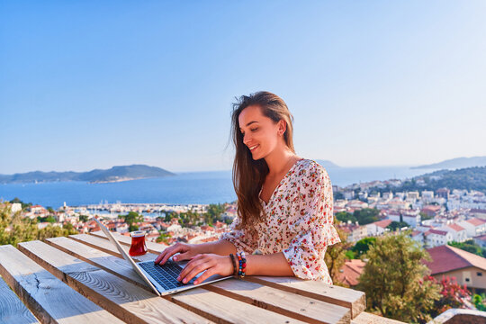 Smiling happy cute young girl traveler remote working at a computer with a beautiful view. Freelance concept
