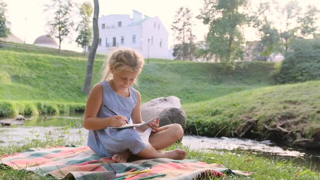a teenage girl draws sitting on the nature near the river.