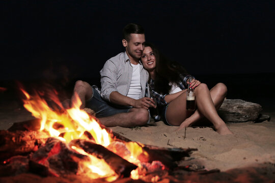 Young couple in love drinking beer from glass bottles on a campfire background