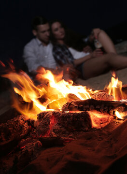 Blurred young couple in love drinking beer from glass bottles on a campfire background