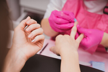 Manicure salon master leaks female nails with a lint free napkin in a nail salon. Woman getting nail manicure. Professional manicure in beauty salon. Care for hands. - 527082815